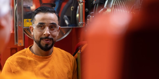 A man wearing safety glasses standing in front of a large machine in an industrial environment